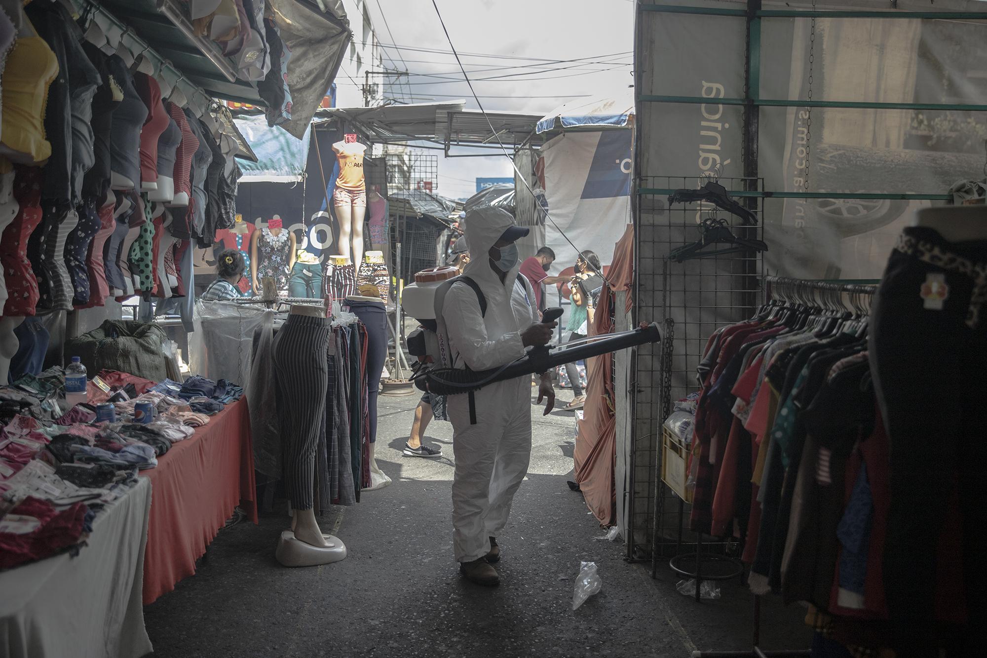 Un empleado de la Alcaldía de San Salvador fumiga una venta de ropa ubicada sobre la calle Rubén Darío. A pesar de que la fase uno no contempla los negocios de venta de ropa, algunos han decidido abrir por la necesidad de obtener ingresos que por más de 80 días dejaron de percibir.