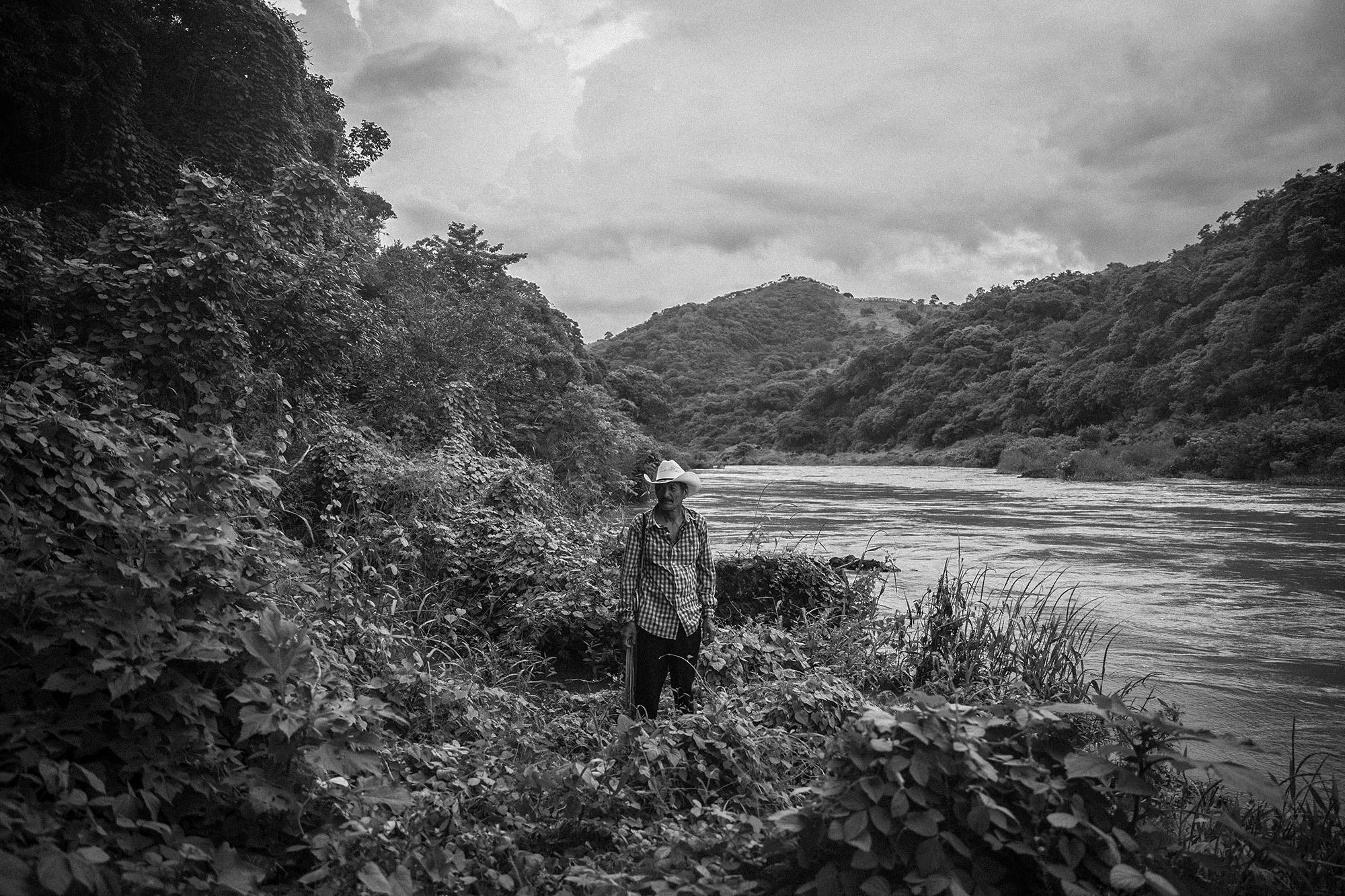 Gerardo Leiva on the banks of the Lempa River, at the site where he helped dozens of people cross on March 18, 1981. He remembers that to get to this point, his “compas” had to fight off the army as people made their way toward Honduras.