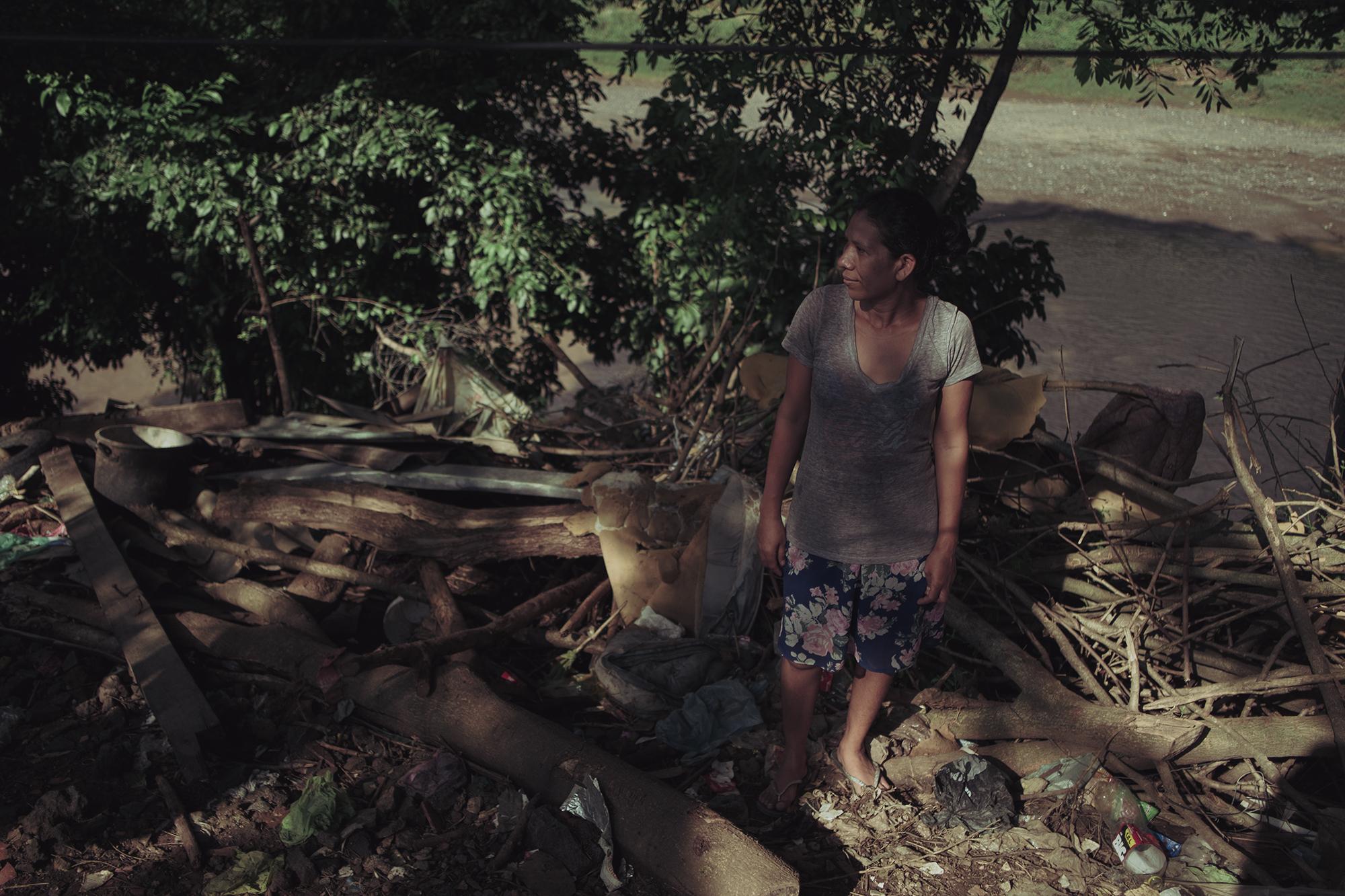 Luz Fuentes in the yard of the property where she has lived for ten years along the Río Grande in Urbina 2, San Miguel. Each swelling of the river has left all sorts of debris at Luz’s home and chewed away at the land where she built her sheet metal home, causing her to flee in search of a more stable spot on level ground farther from the riverbank.  