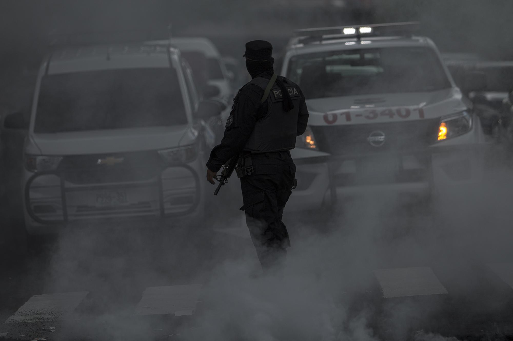 La Policía Nacional Civil custodió la marcha desde el inicio hasta el final. En la imagen, uno de los agentes quedó inmerso entre el humo y la nieve carbónica del extintor de fuego, después de que los manifestantes incendiaran llantas sobre el Bulevar Universitario.