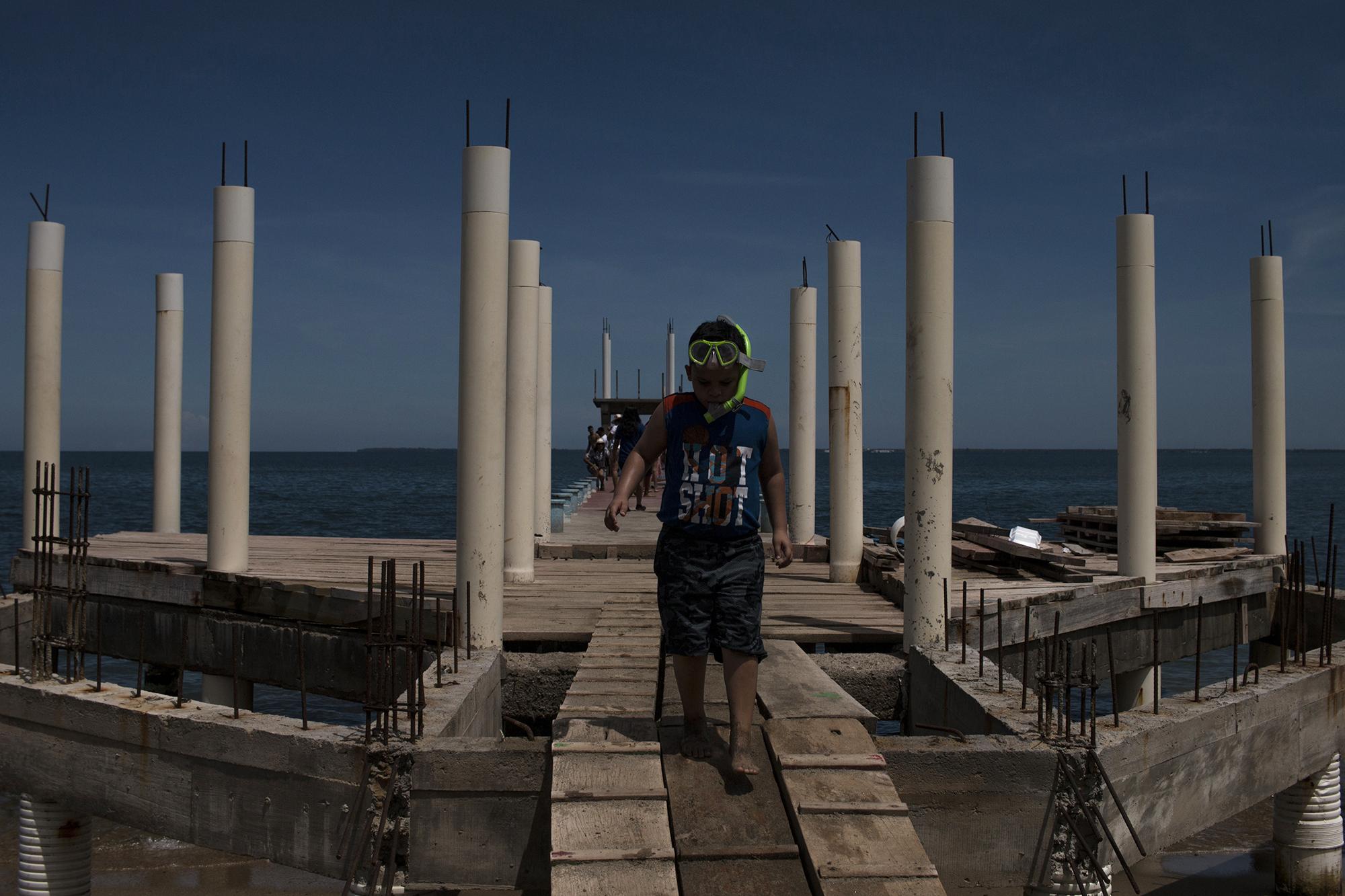 Dylan Alexander Banegas, de 7 años, juega con su equipo de esnórquel, en medio de una construcción a medio andar sobre el muelle de la bahía de Trujillo, departamento de Colón, en el Caribe de Honduras. Foto de El Faro: Víctor Peña.