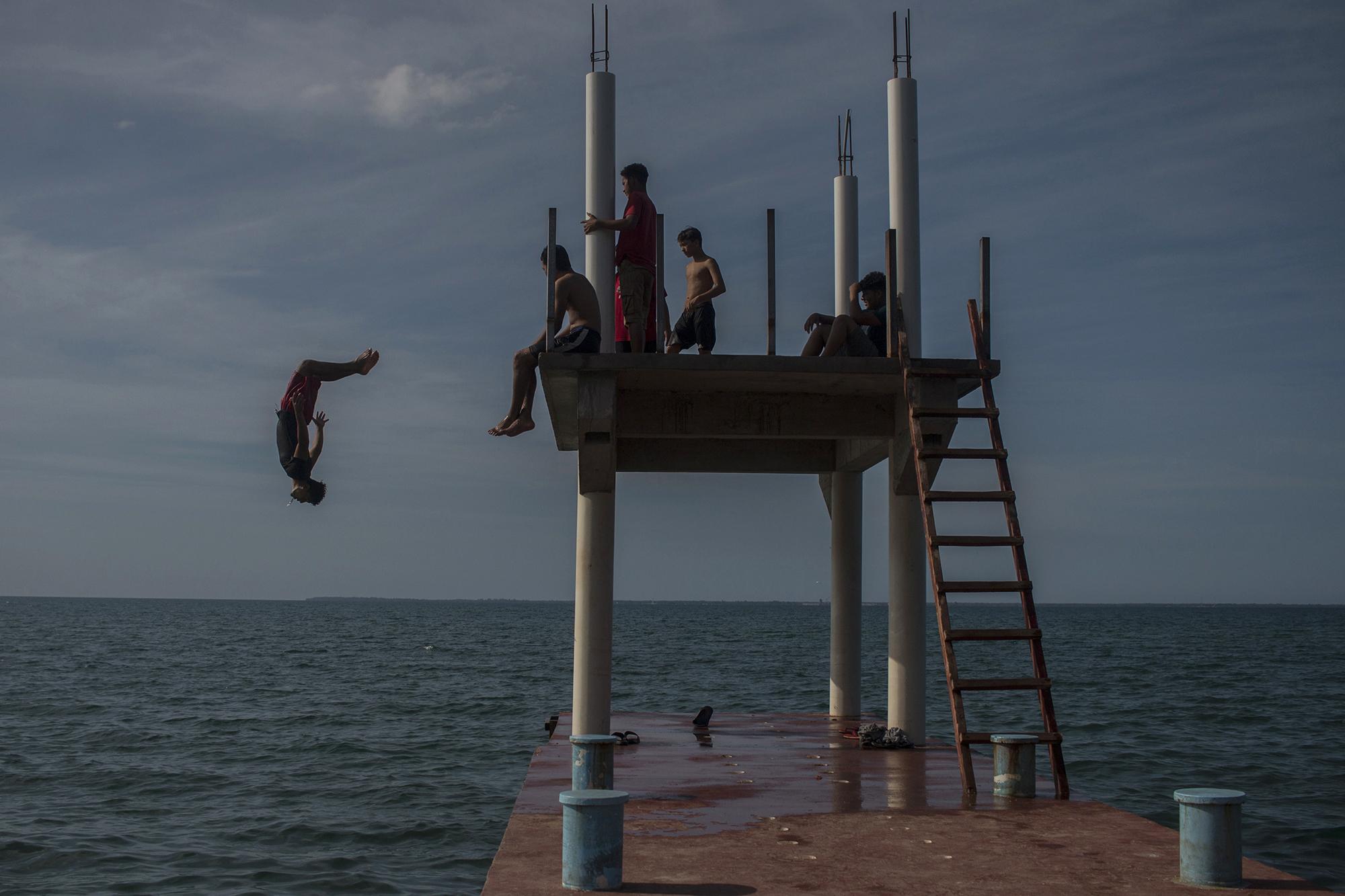 Local children jump from the dock into Trujillo Bay, one of the few distractions for youngsters living nearby. Photo: Víctor Peña/El Faro