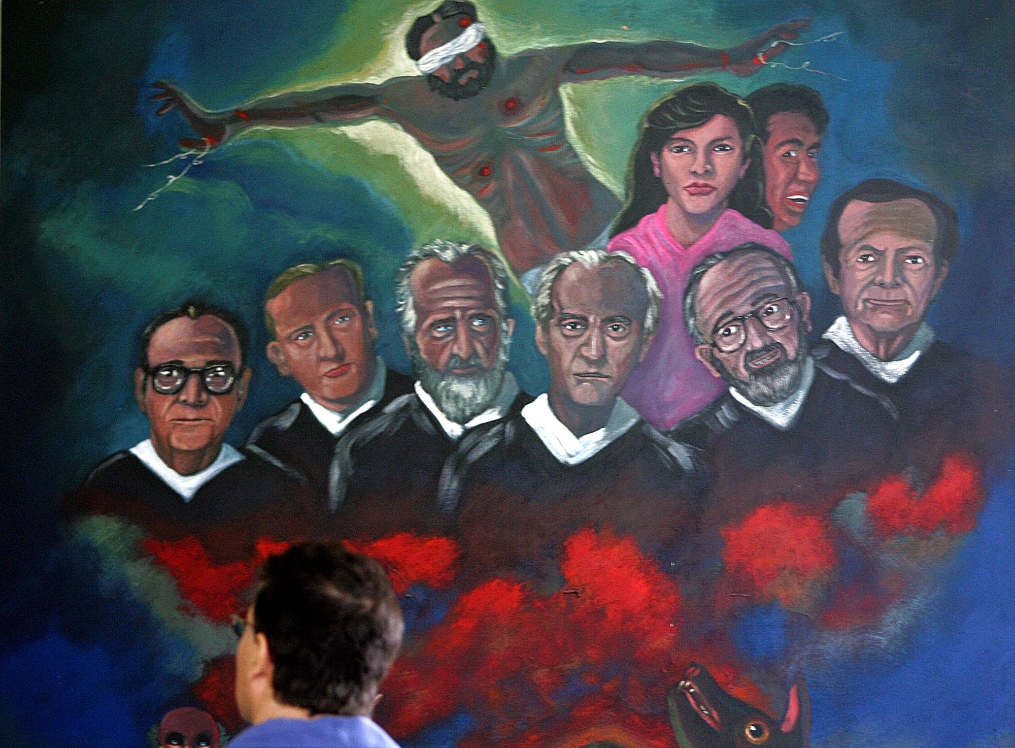 On November 16, 2006, on the 17th anniversary of the murder of six Jesuit priests and two collaborators, a man observes a mural in the Central American University (UCA) chapel depicting their faces. That day, dozens congregated near the tomb of the martyrs as the UCA called on authorities to bring the intellectual authors of the crime to justice. Photo Yuri Cortez/AFP