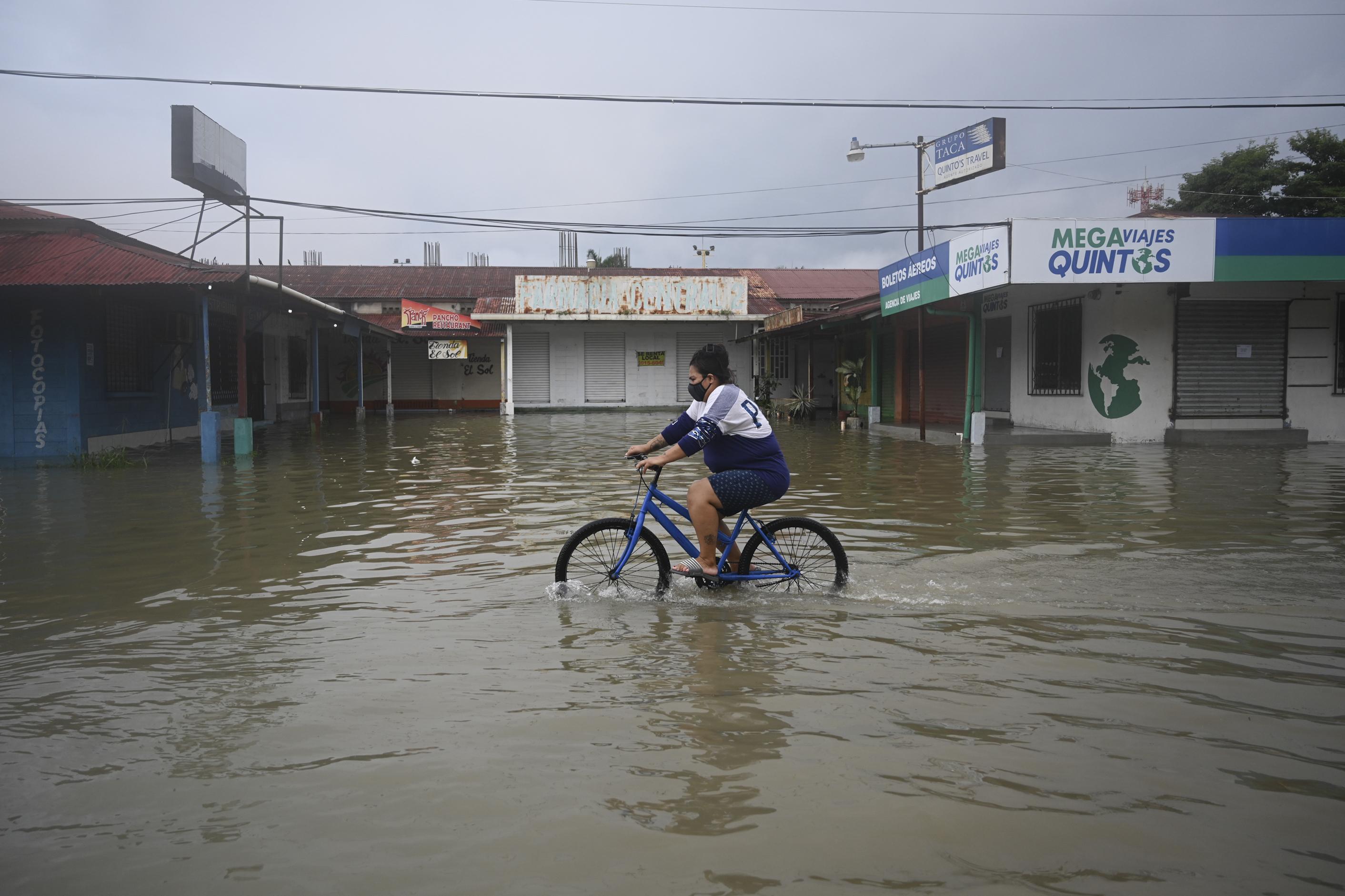 Una mujer anda en bicicleta en una calle inundada debido a las fuertes lluvias provocadas por el huracán Eta, ahora degradado a tormenta tropical, en Puerto Barrios, Izabal 310 km al norte de la Ciudad de Guatemala. Foto de Johan Ordoñez / AFP.