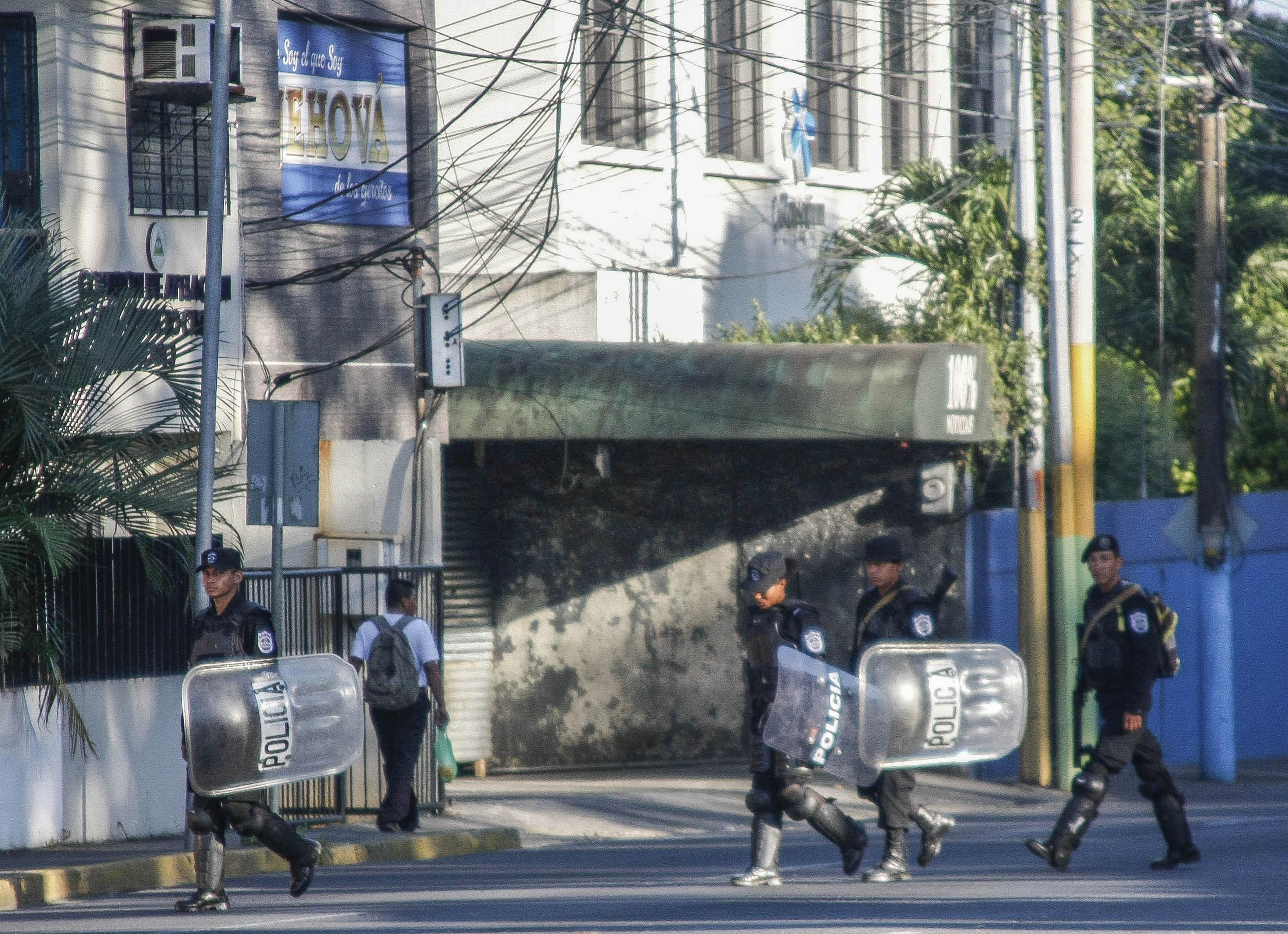 Policías orteguistas patrullan frente a la sede de 100% Noticias