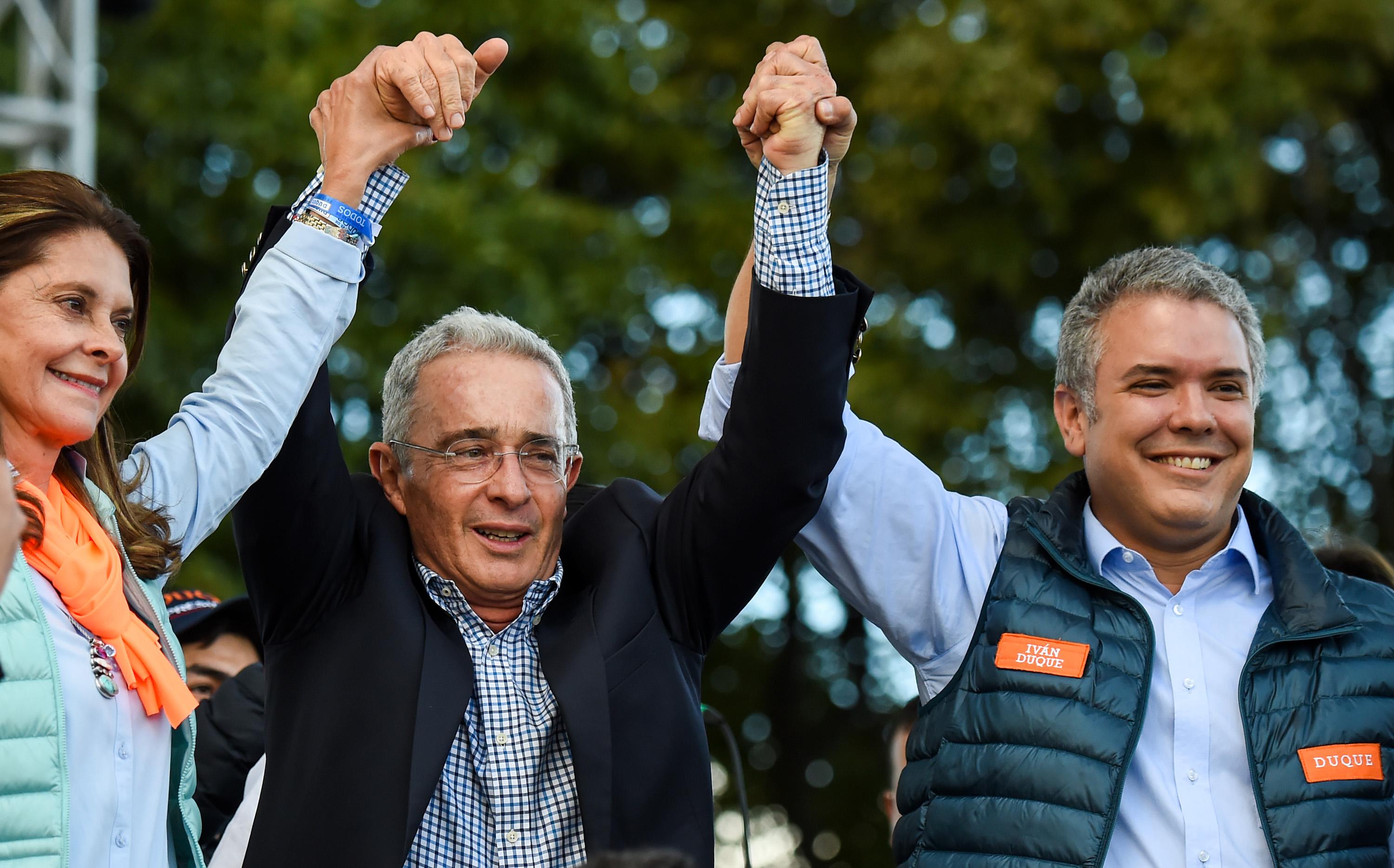 El expresidente de Colombia Álvaro Uribe (centro) alza la mano del presidente electo Iván Duque, del Centro Democrático, en un mitin del 20 de mayo de 2018. Uribe se alejó de eventos públicos con Duque en la última parte de la campaña. Foto AFP/ Raul Arboleda
