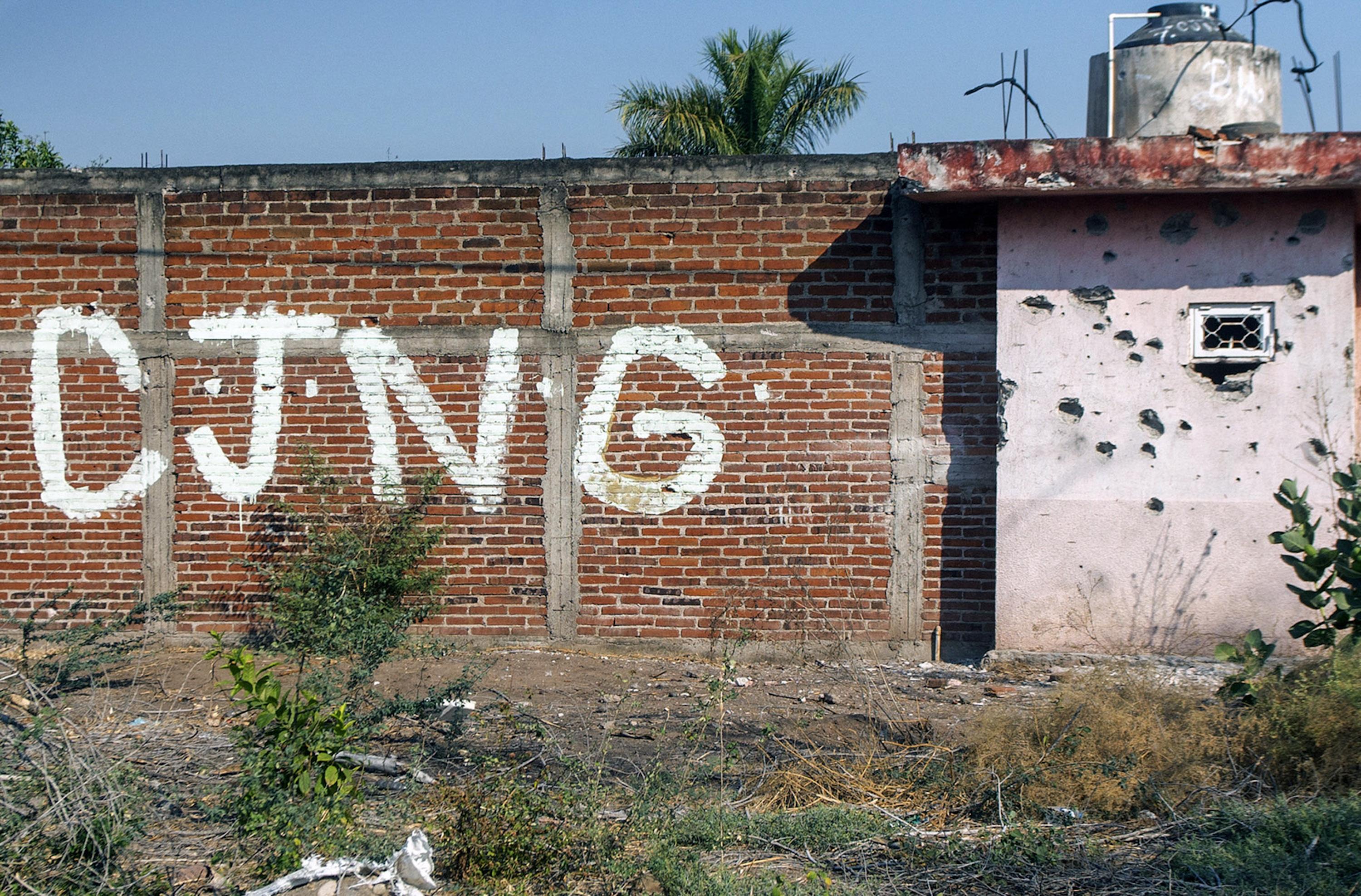A bullet-riddled wall with the initials of the Jalisco New Generation Cartel at the entrance to the community of Aguililla, in the Mexican state of Michoacán, on Apr. 23, 2021. The community is besieged by a battle between CJNG and the Familia Michoacana, also known as Viagras. Photo: AFP