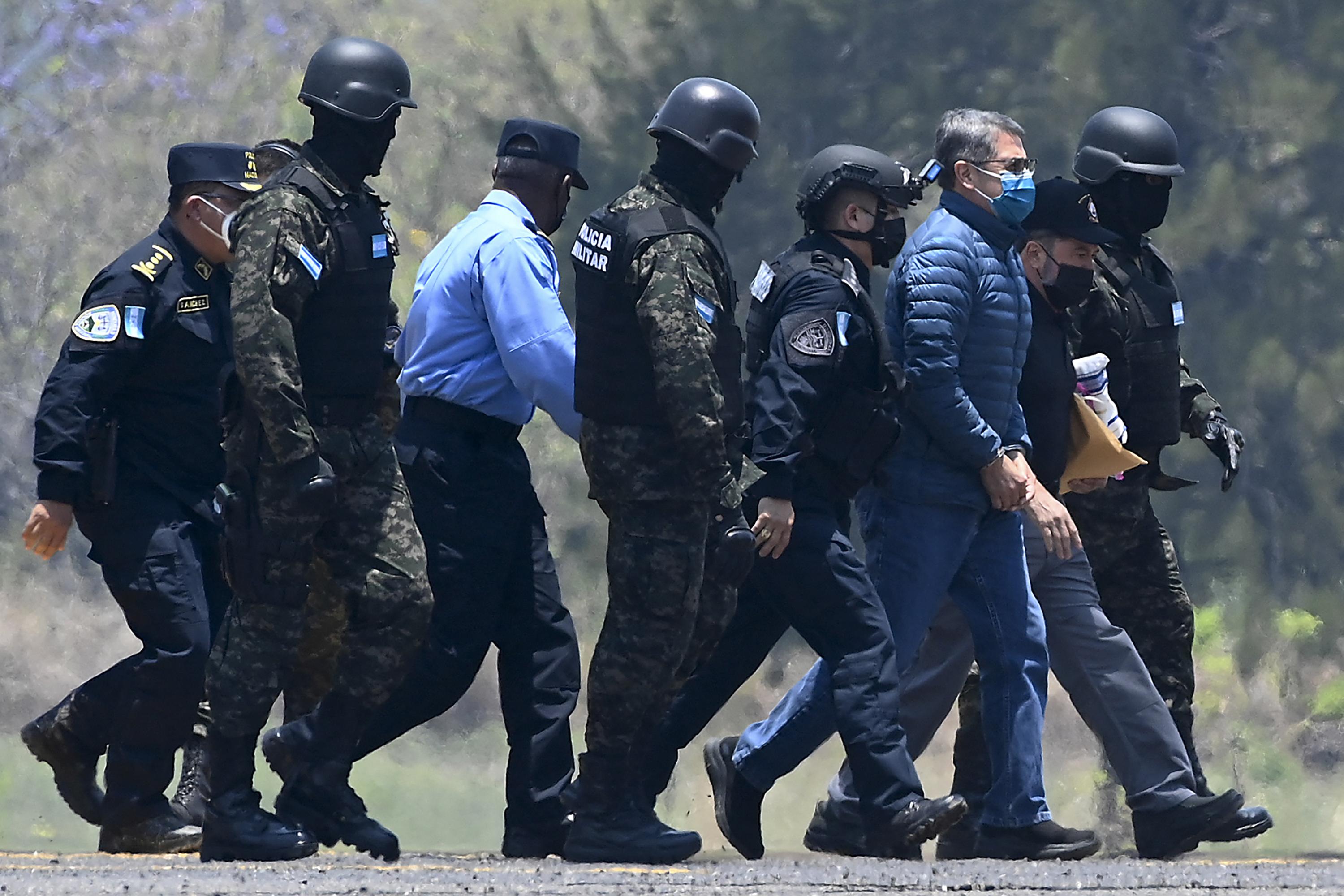 Juan Orlando Hernández es escoltado por agentes policiales a su llegada a una base de la Fuerza Aérea en Tegucigalpa. Una imagen del 21 de abril de 2022, antes de su extradición a Estados Unidos, donde enfrenta cargos relacionados con el narcotráfico. Foto de El Faro: Orlando Sierra/ AFP.