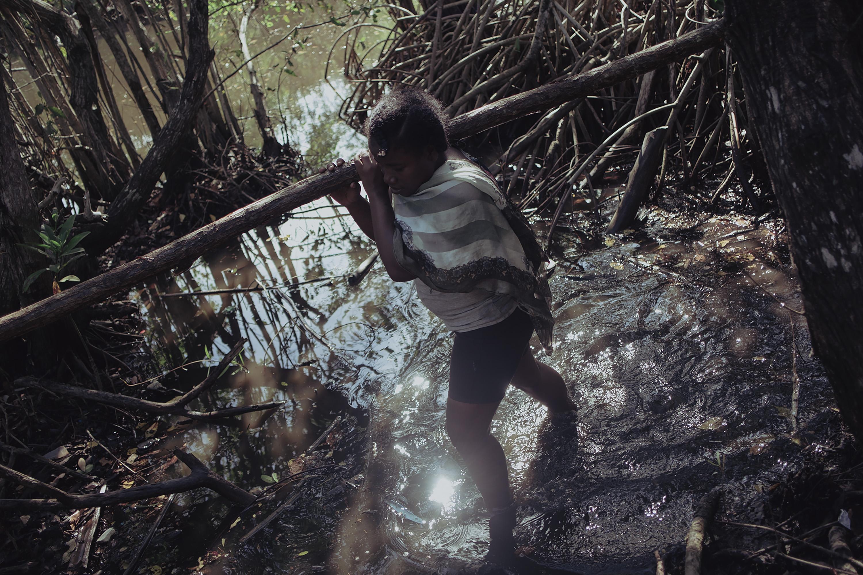 Clenny David, 34, wades through swampland in a patch of Garifuna ancestral land called Africa, where men and women from Nueva Armenia gather wood from fallen trees to build ancestral health clinics. Soaked in the humid heat, the men chop wood while the women carry it to rafts to be transported to the community.