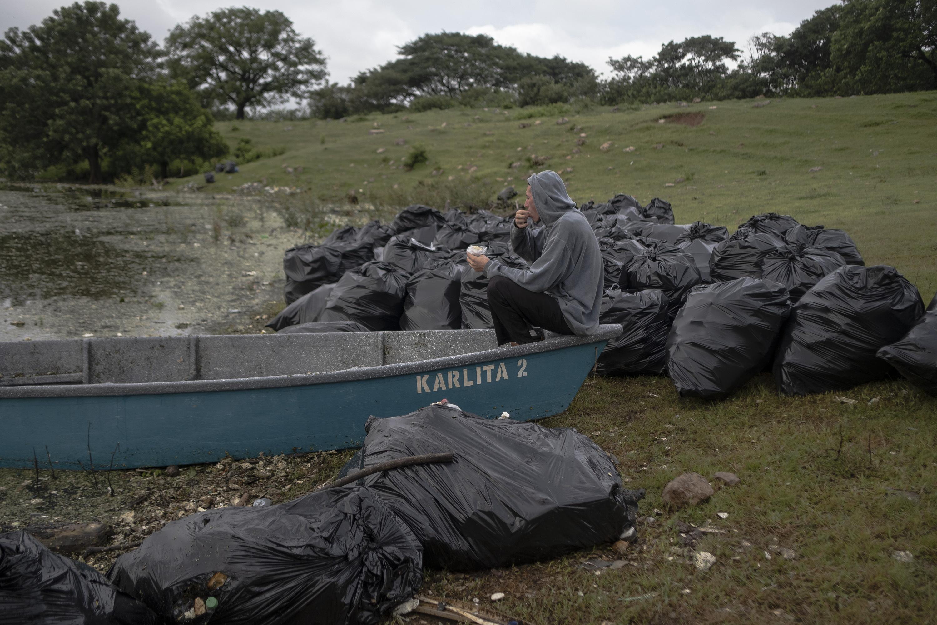 Óscar Menjívar, 45, eats his breakfast in a boat surrounded by bags full of garbage on the shore of the Cerrón Grande reservoir. Since the waste has polluted the water, his workdays as a spearfisherman have been reduced: “Spearfishing is impossible. In order to shoot, you must be able to see your target, and the garbage has created a layer so thick that not even light enters the water in many places,” he said.