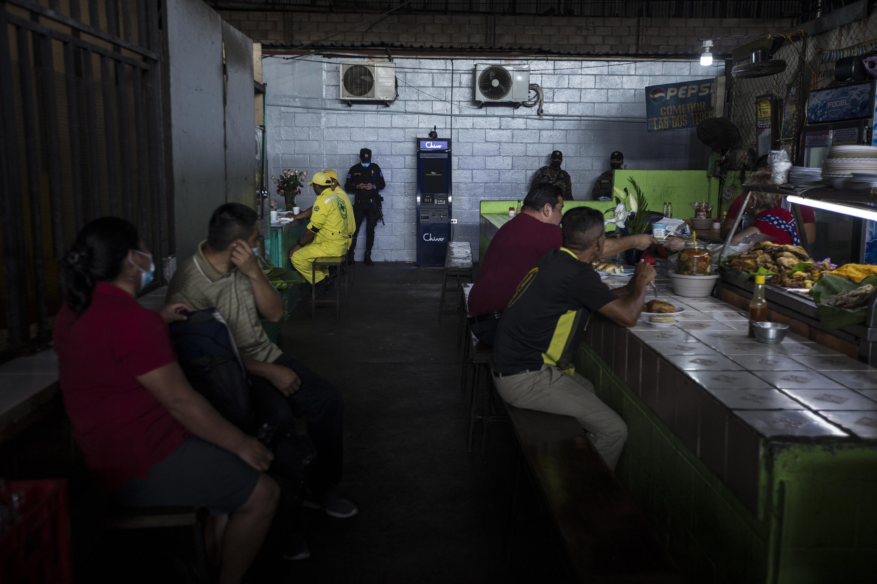 Two soldiers and a police officer watch over the Chivo ATM in the lunchroom in the Central Market of Santa Tecla. Photo: Víctor Peña/El Faro