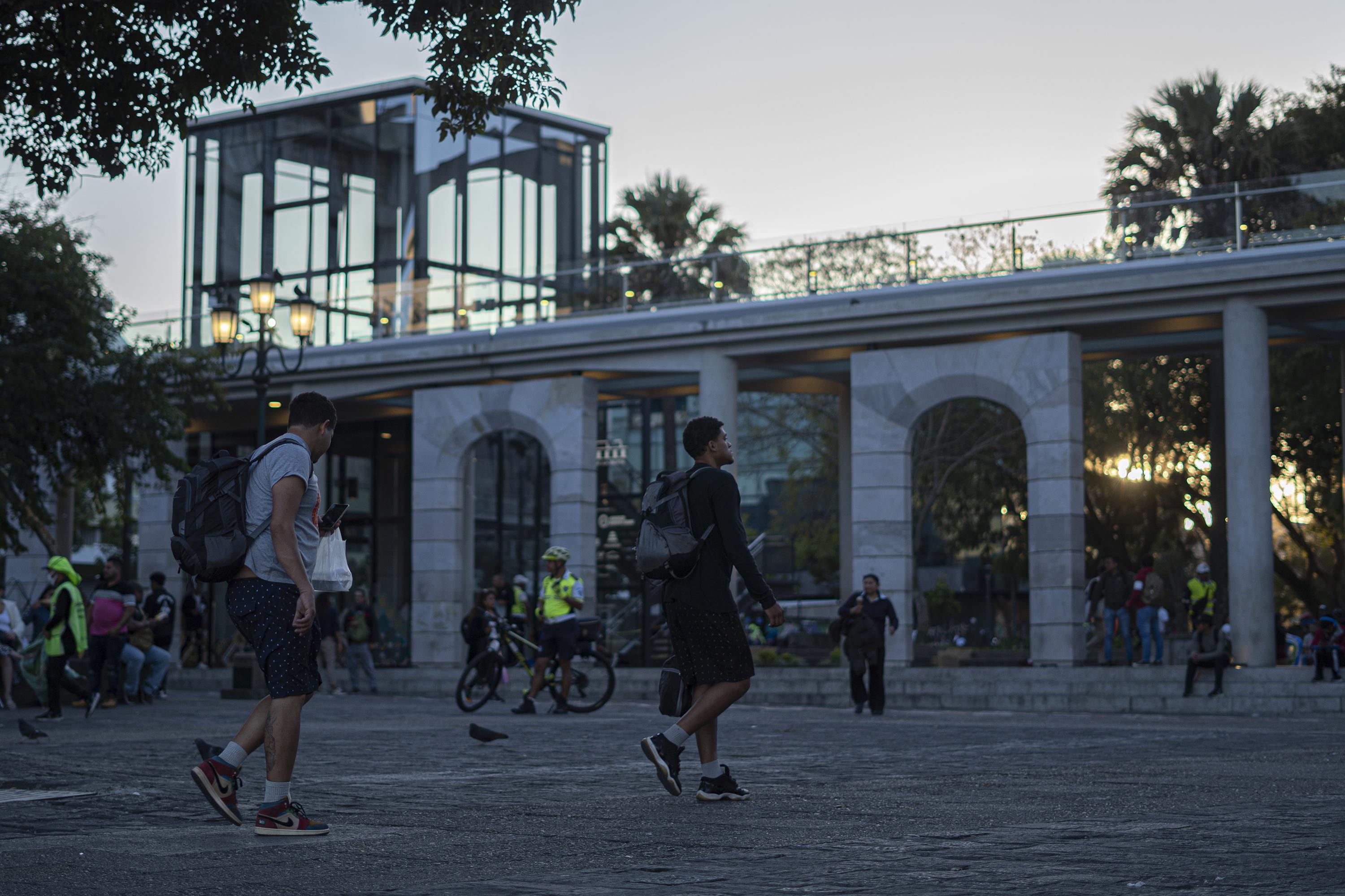 John (left) and Yoiner, 23 and 20 years old, respectively, cut through Constitution Plaza in the center of Guatemala City on their way to their hotel after a long day of asking for money for eight hours. Childhood friends from the heart of Caracas, one left the country in 2017 and the other in 2022. They reunited on their way to the United States. Photo: Víctor Peña/El Faro