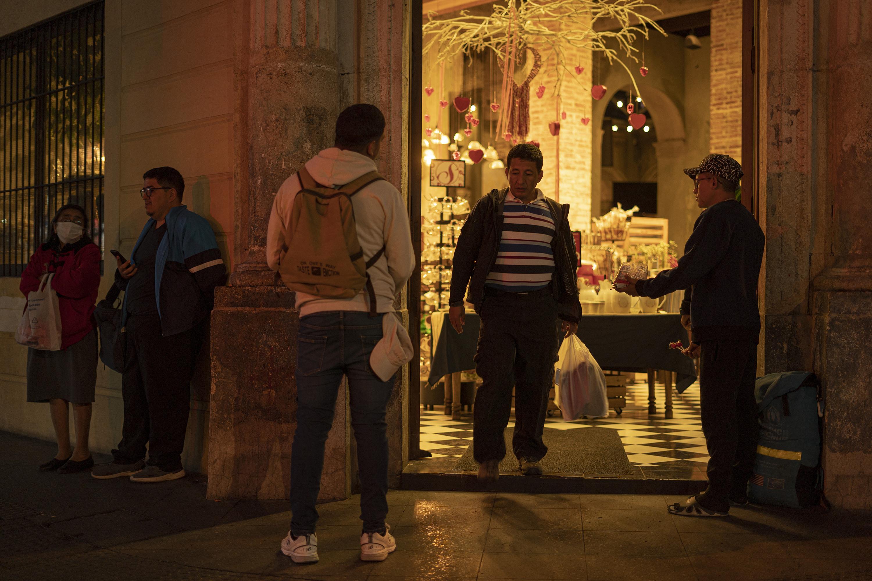 Leonardo Caguana and Juan ask for money and sell candies in front of the San Martín bakery on Sixth Avenue. Venezuelan migrants have become a daily presence on this street corner. Photo: Víctor Peña/El Faro