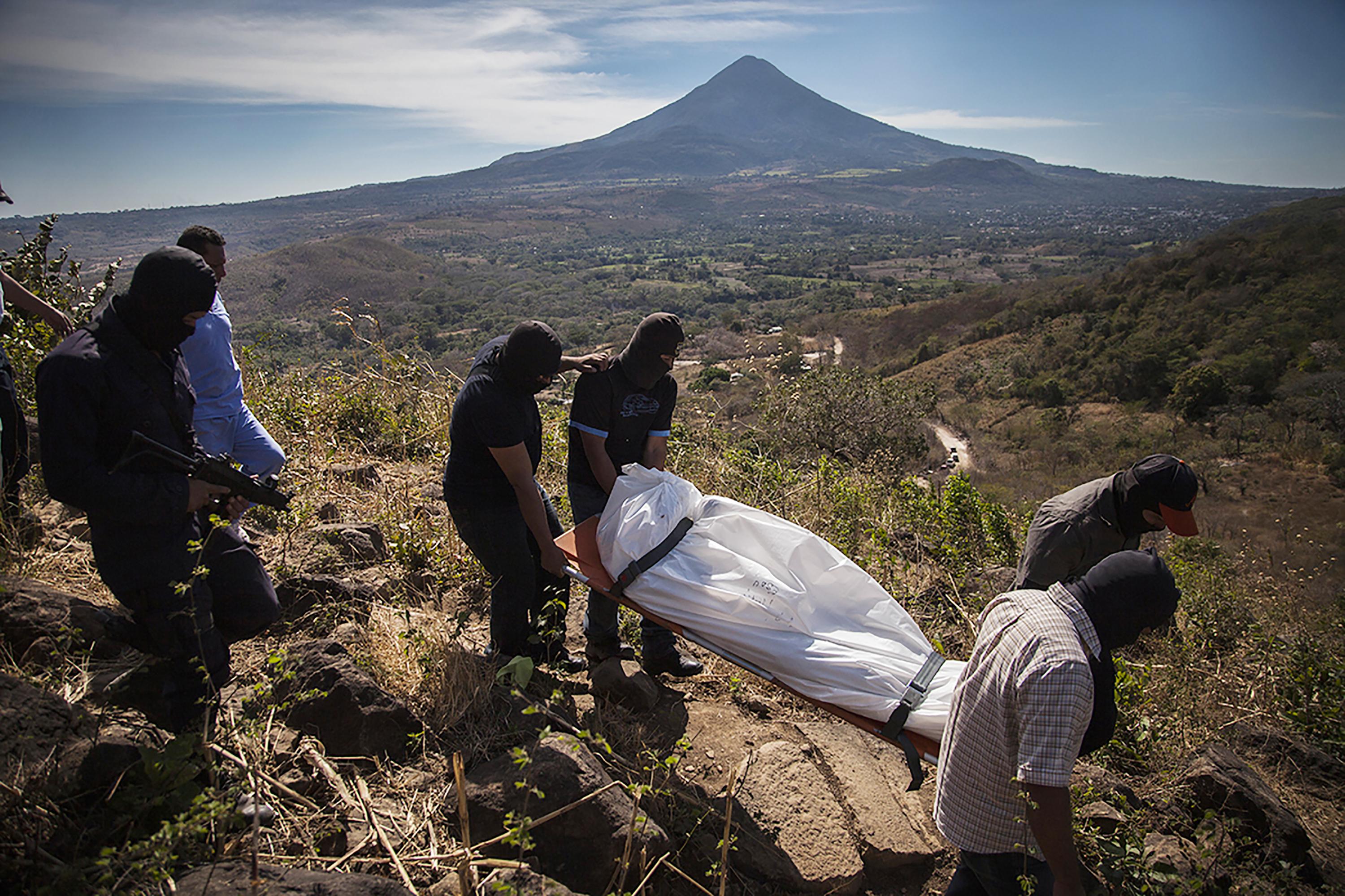 Police officers remove the body of a National Civil Police agent who died in a shootout with gang members on February 9, 2016 on the Cutumayo hill in San Vicente. Behind them is the Chichontepec Volcano. Photo: Víctor Peña/El Faro