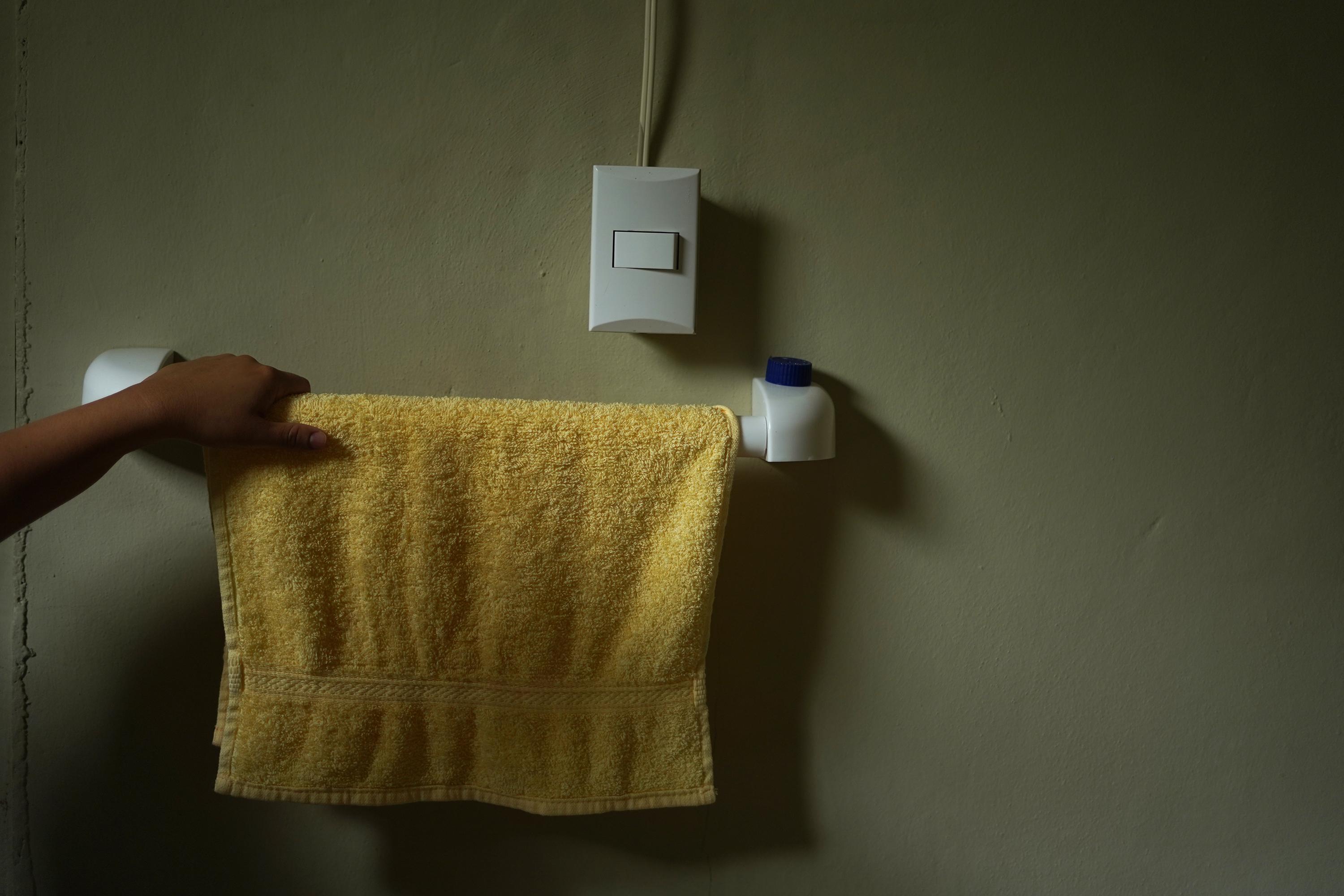 Lorena rests her hand on a towel rack in the bathroom of the hotel where she and her family have taken refuge, to avoid being arrested under El Salvador’s state of exception. Photo: Víctor Peña/El Faro