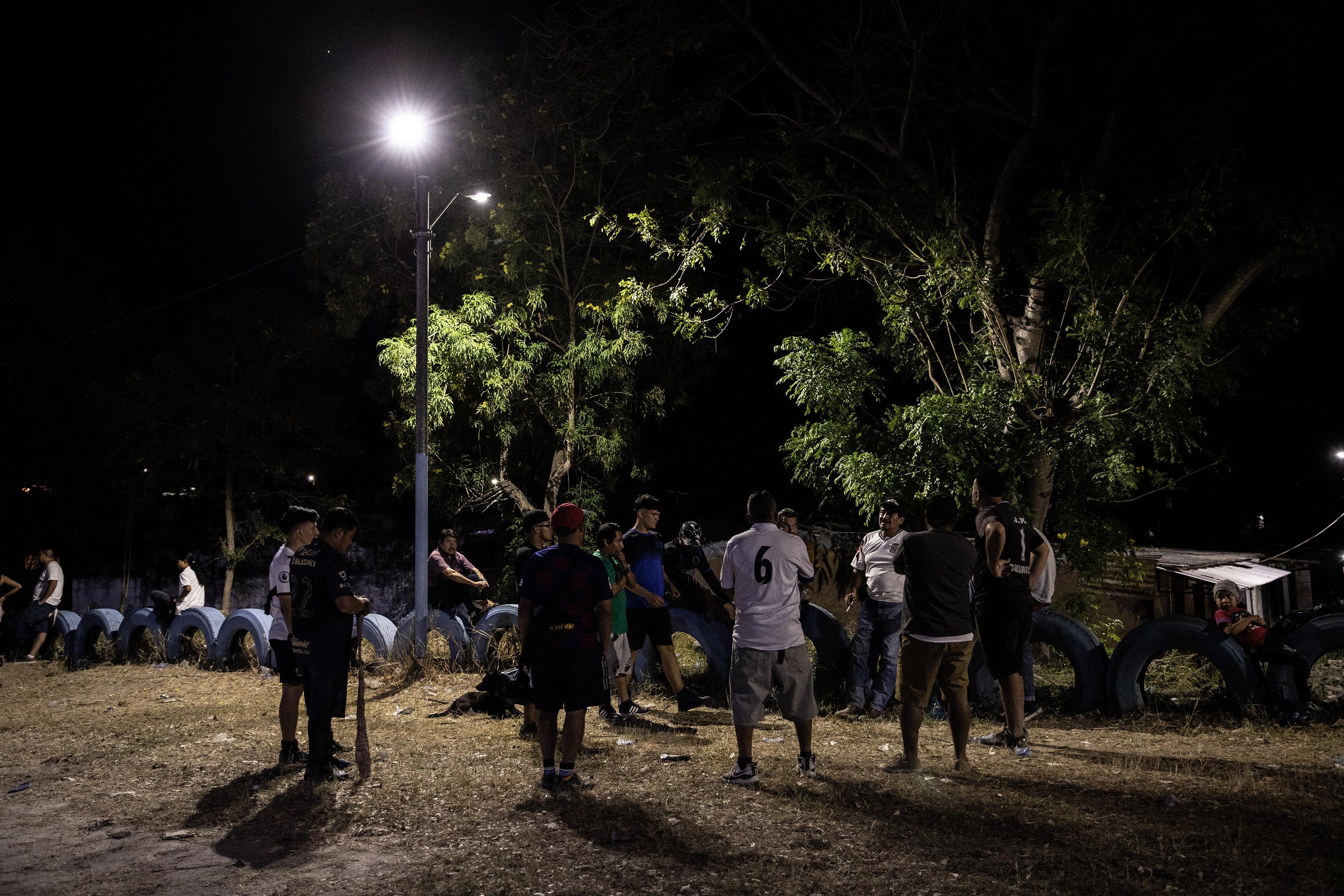 Standing under the glow of a streetlamp, the Las Cañas sports committee discusses team agreements for the soccer tournament they are organizing to unite youth from both sides of their divided community. Photo: Carlos Barrera/El Faro