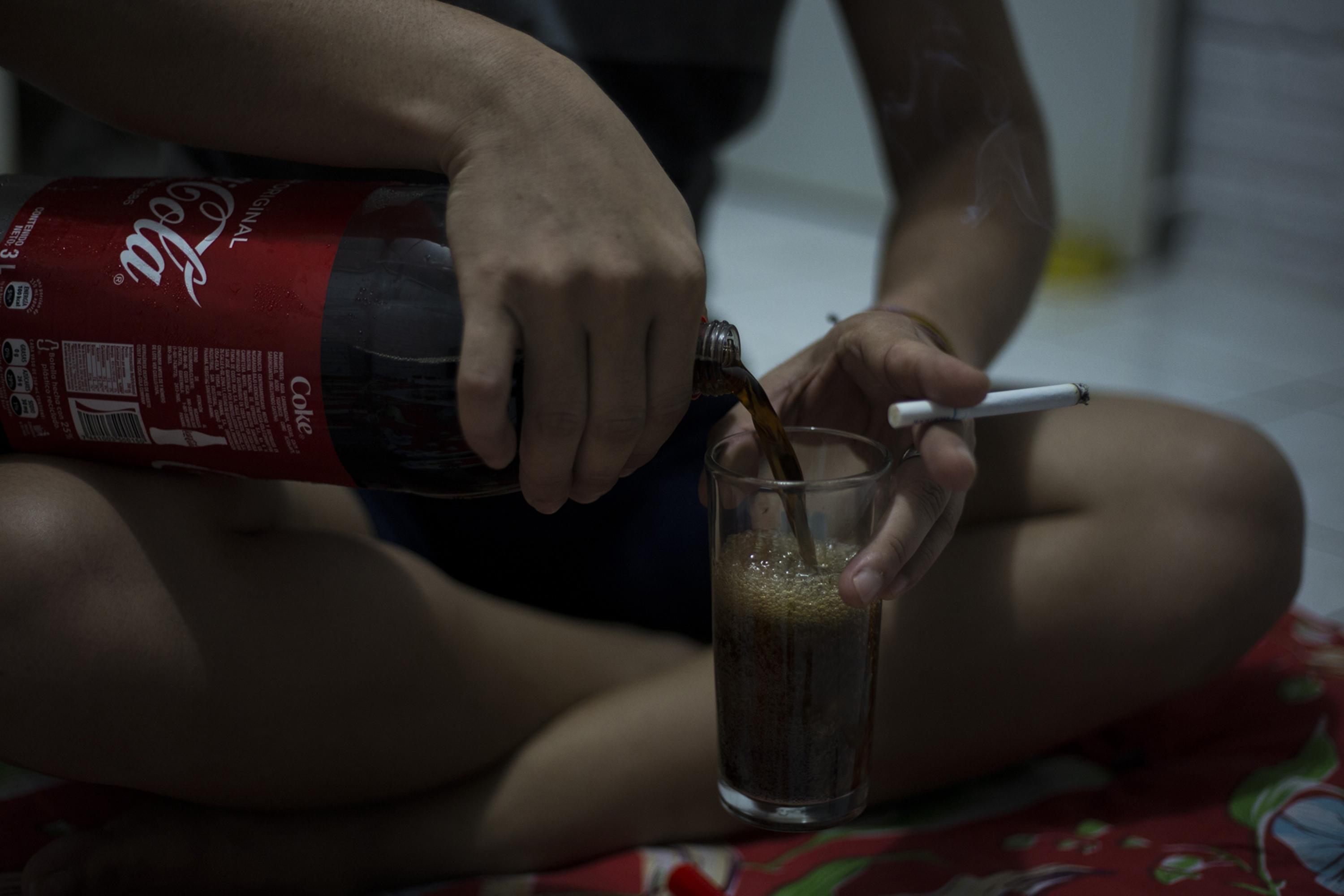Doctor Veneno,one of those taking refuge in the safe house, pours himself a glass of Coke and lights a cigarette to speak with his student comrades, as they often do to pass the time. Photo Víctor Peña
