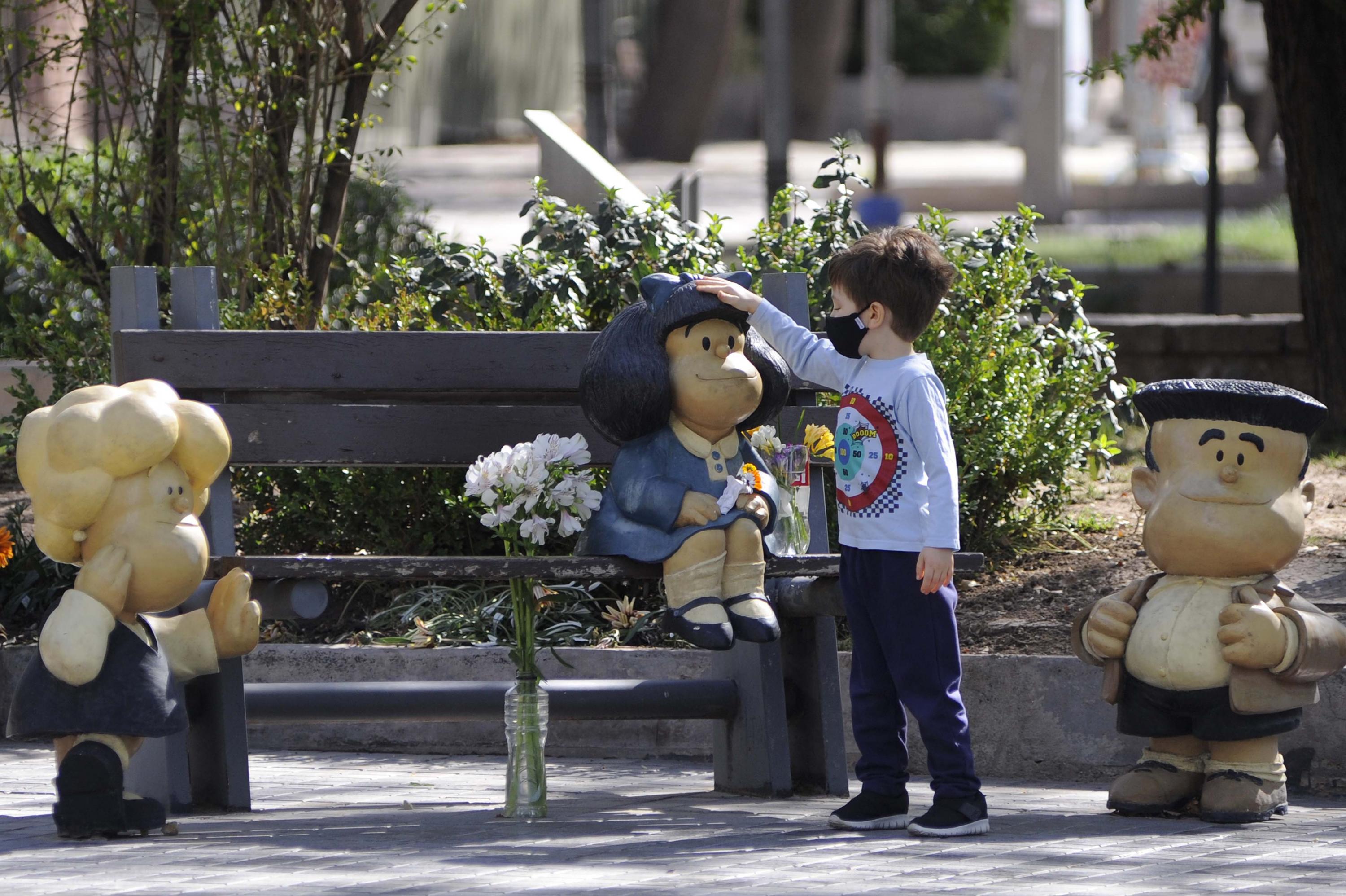Un niño acaricia una estatua de Mafalda flanqueada por ramos florales en Mendoza, Argentina, este 30 de septiembre. Foto de Andres Larrovere / AFP.