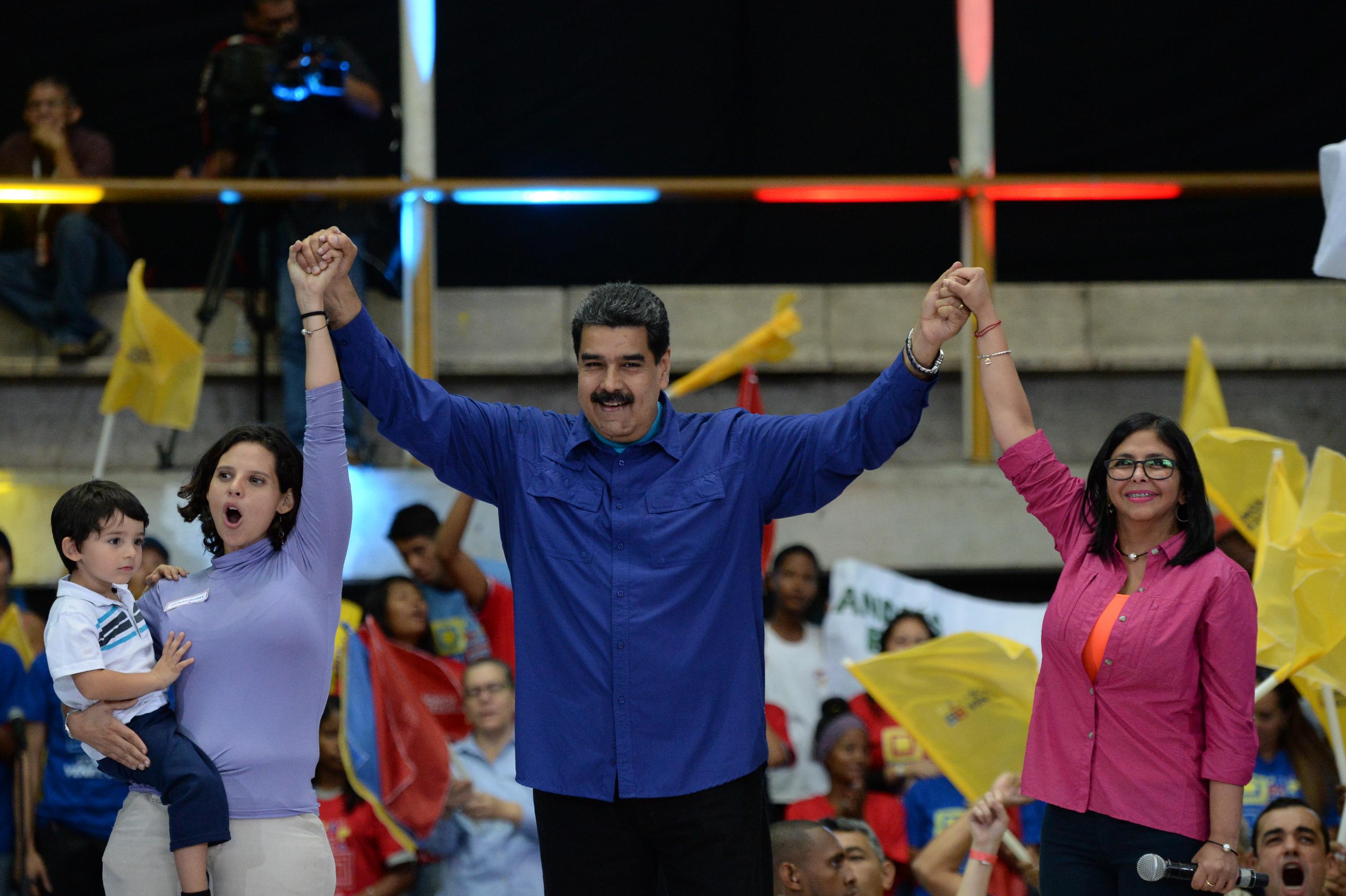 Venezuelan President Nicolas Maduro (C), the head of the Constituent Assemby, Delcy Rodriguez (R) and a supporter raise hands during a rally in Caracas on February 7, 2018. Maduro launched Wednesday a political movement to promote his candidacy for reelection. / AFP PHOTO / FEDERICO PARRA