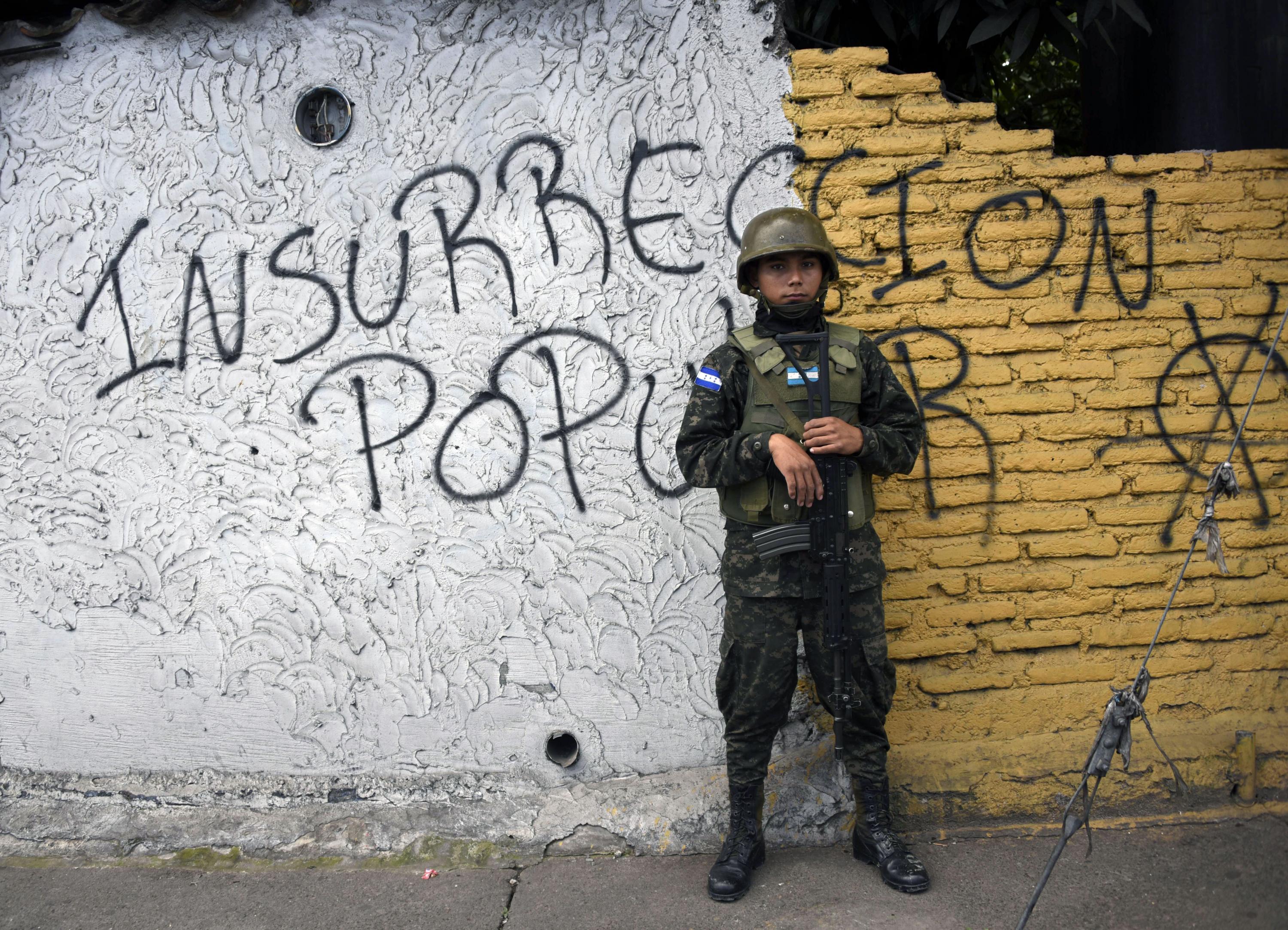 An Honduran Army soldier stands guard in front of a graffiti reading 