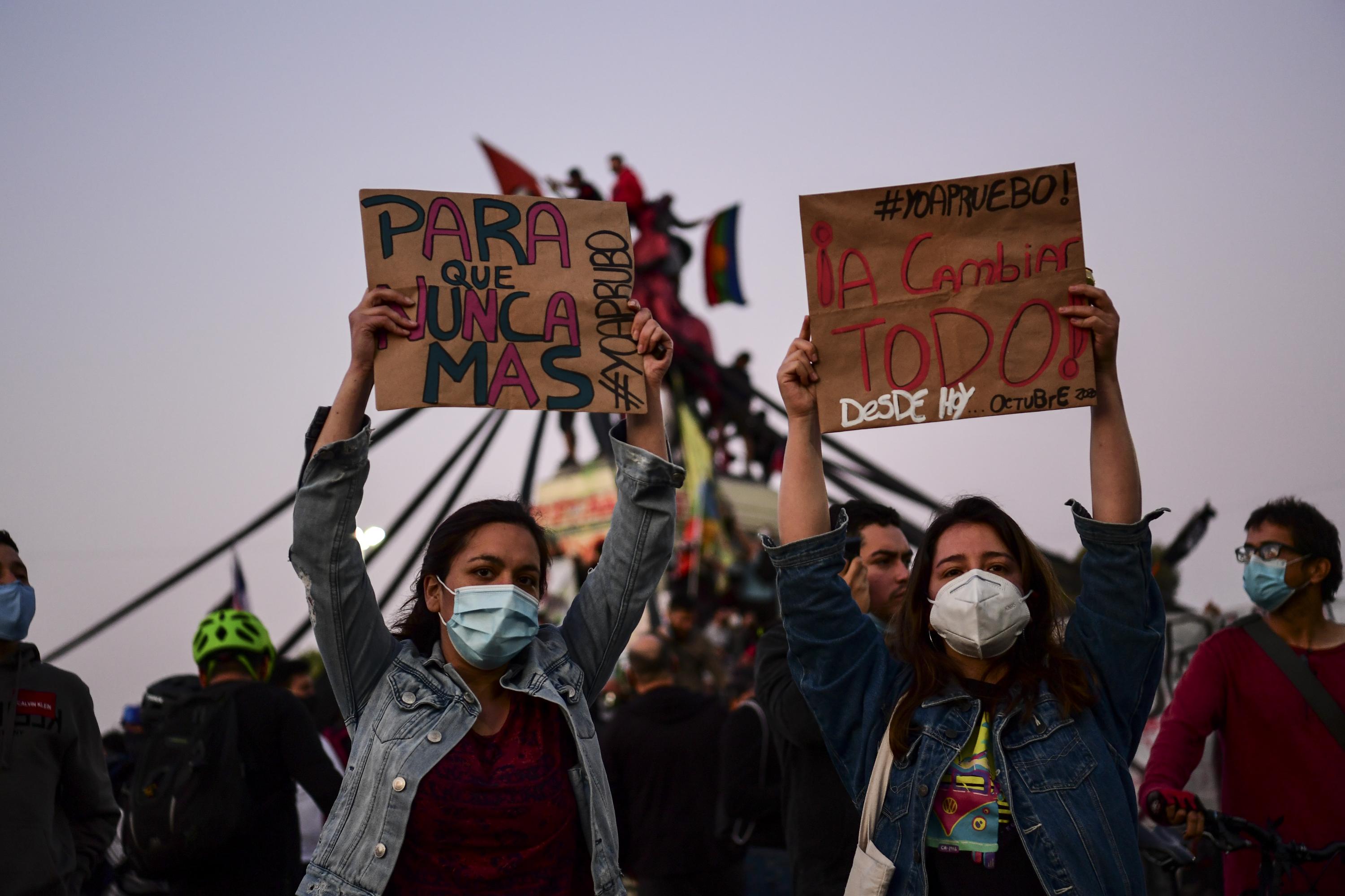 Dos jóvenes levantan carteles de apoyo al cambio de Constitución. El hito de este domingo en Chile, para algunos, es la conclusión de las protestas por una sociedad más igualitaria impulsadas desde la calle por jóvenes estudiantes. Foto de MARTIN BERNETTI / AFP.