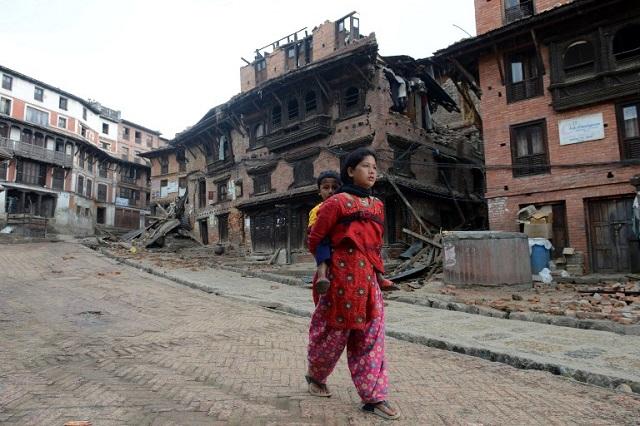 Una mujer nepalí carga a un niño contiguo a unas casas que colapsaron con el terremoto de 7.8 grados, en Bhaktapur, en las afueras de Katmandú. Hasta el 27 de abril se habían registrado 4 mil personas fallecidas. AFP PHOTO / PRAKASH MATHEMA