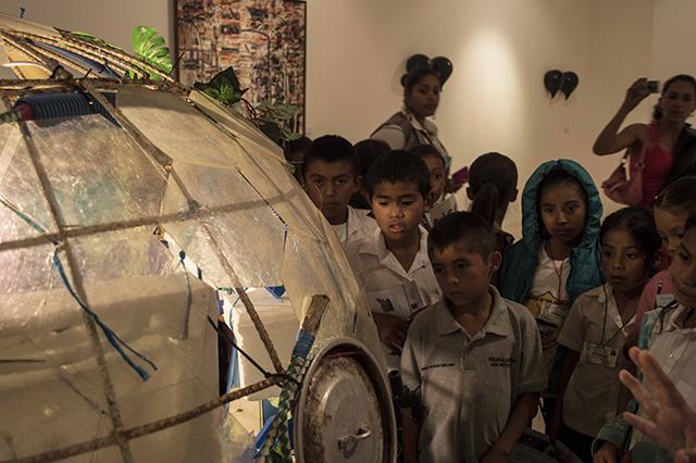 Niños del centro escolar Hibueras observan con detenimiento los materiales reciclados que utilizó el artista para construir su cápsula espacial.