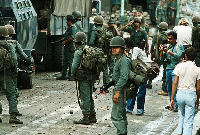 1982. Militares se preparan para abordar vehículos blindados antes de ser emboscados en San Vicente. A la derecha, de bigote con cámara, el fotoperiodista salvadoreño Luis Romero. Atras de él el 