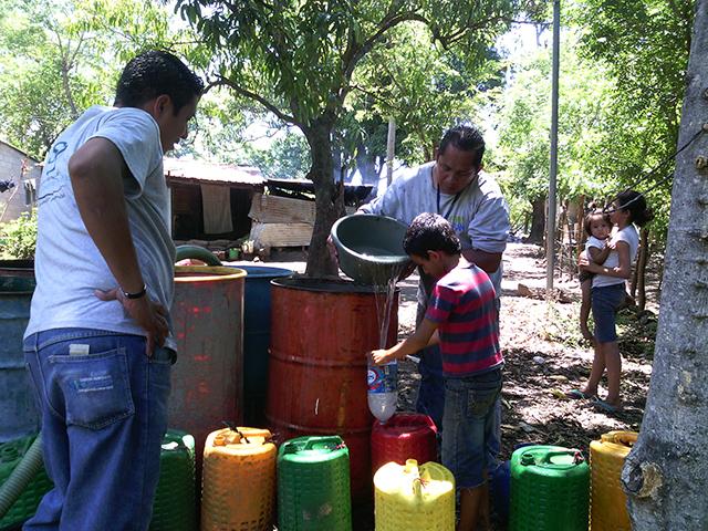 Un niño del cantón El Palomar de San José Villanueva llena varios barriles y huacales con el agua de la pipa donada por El Encanto. 
