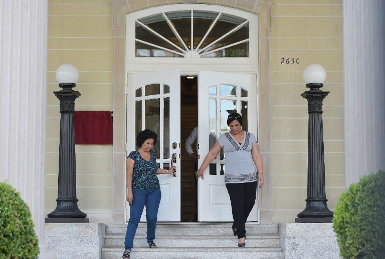 Dos mujeres ensayan la apertura de puertas de la Oficina de intereses económicos de Cuba en Washington un día antes que Estados Unidos y Cuba rehabiliten las relaciones diplomáticas que se cortaron hace medio siglo. La oficina de intereses económicos de Cuba se convertirá, como parte de la nueva era diplomática, en embajada. Foto de AFP/MANDEL NGAN.