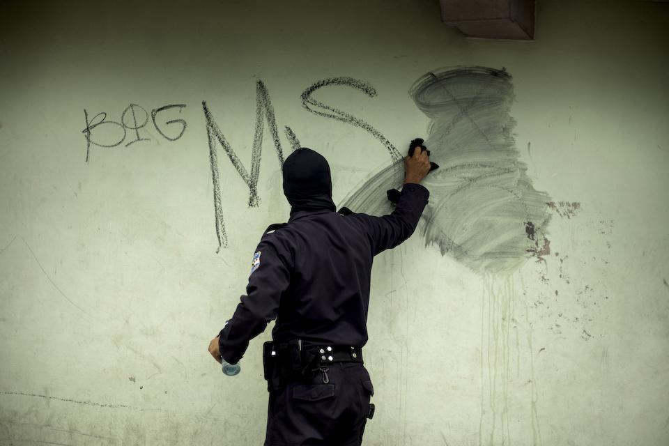 Un agente de la PNC borra un grafiti de la Mara Salvatrucha (MS) en el centro de Zacatecoluca. Hasta le fecha, la MS se ha mantenido al margen de la batalla que las dos facciones del Barrio 18 sostienen en el municipio. En El Salvador, borrar un grafiti de una pandilla puede costar la vida, ya que usualmente las pandillas lo interpretan como una falta de respeto.